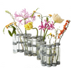 A set of modern cylindrical glass vases with metallic silver bands, filled with an assortment of colorful artificial flowers, including pink, yellow, orange, and white blossoms, on a solid white background.