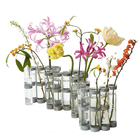 A set of modern cylindrical glass vases with metallic silver bands, filled with an assortment of colorful artificial flowers, including pink, yellow, orange, and white blossoms, on a solid white background.