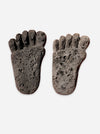 A pair of dark gray, textured lava stone foot-shaped pumice stones on a light gray background.