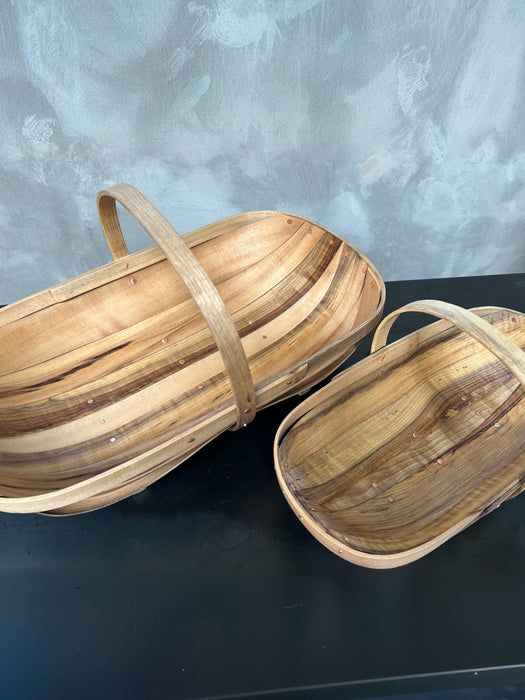 Two handcrafted woven wooden baskets with curved handles, displayed on a dark surface against a textured gray background.