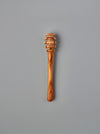 A single wooden honey dipper with a carved slotted head and smooth handle, shown vertically against a plain gray background.