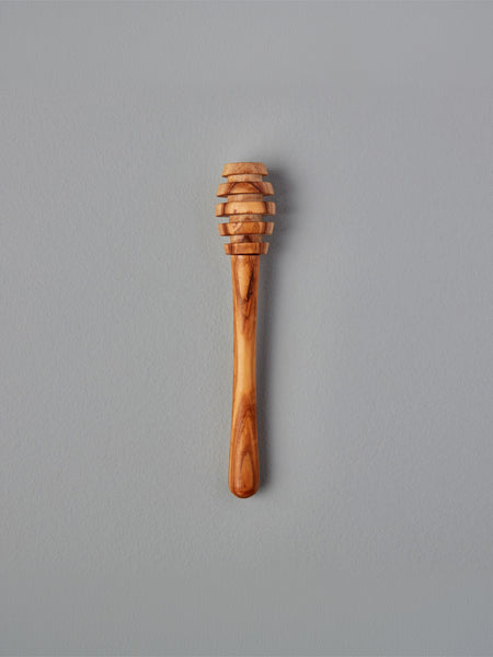 A single wooden honey dipper with a carved slotted head and smooth handle, shown vertically against a plain gray background.