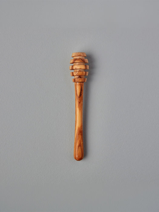 A single wooden honey dipper with a carved slotted head and smooth handle, shown vertically against a plain gray background.
