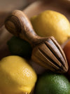 A close-up of a wooden citrus juicer resting on yellow and green lemons in a shallow depth-of-field shot.