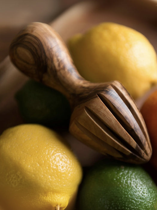 A close-up of a wooden citrus juicer resting on yellow and green lemons in a shallow depth-of-field shot.