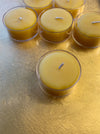 Five small beeswax tea lights in clear glass holders arranged on a textured gold surface.