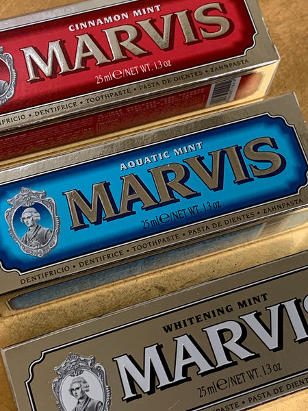 Three Marvis toothpaste tubes stacked diagonally, showing Cinnamon Mint in red, Aquatic Mint in blue, and Whitening Mint in beige packaging.