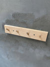 wooden peg hook rack made of light birch wood on a cement grey background.