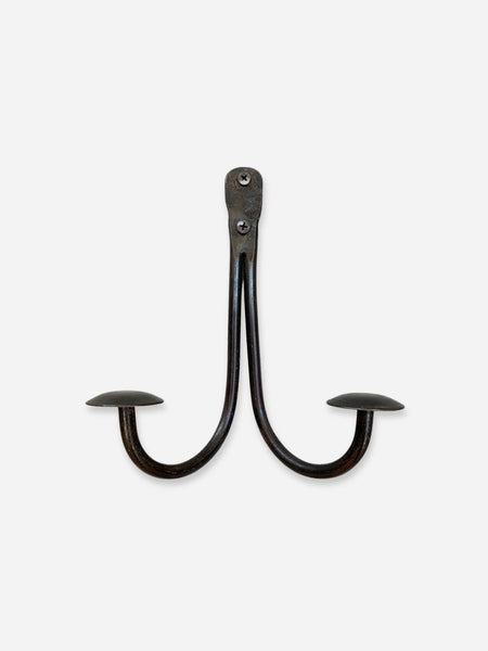 A dark metal two-hook wall hook with a rustic, weathered finish, shown against a plain light gray background.