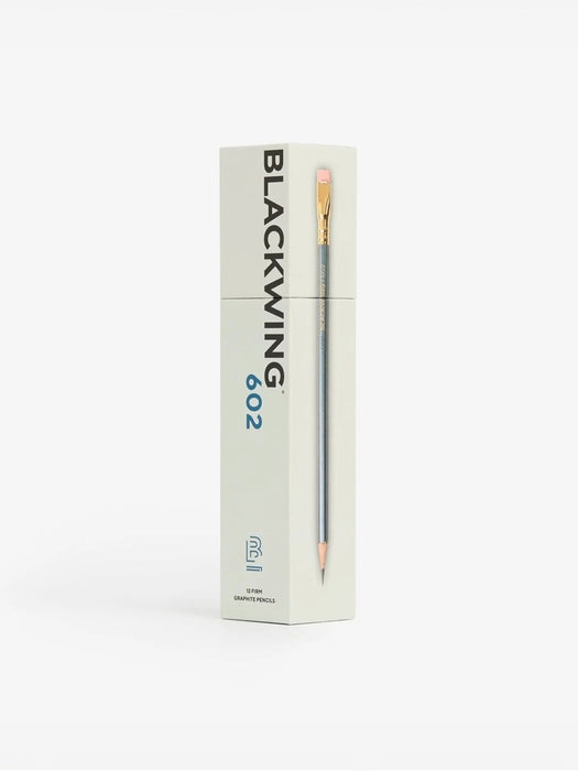 A single Blackwing 602 graphite pencil standing upright next to its tall, off-white packaging box on a clean white background.