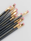 A set of black calligraphy pencils with gold ferrules and pink erasers, arranged diagonally on a light gray background. The pencils feature gold text that reads 'BLACKCROWING CO.
