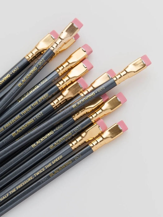 A set of black calligraphy pencils with gold ferrules and pink erasers, arranged diagonally on a light gray background. The pencils feature gold text that reads 'BLACKCROWING CO.