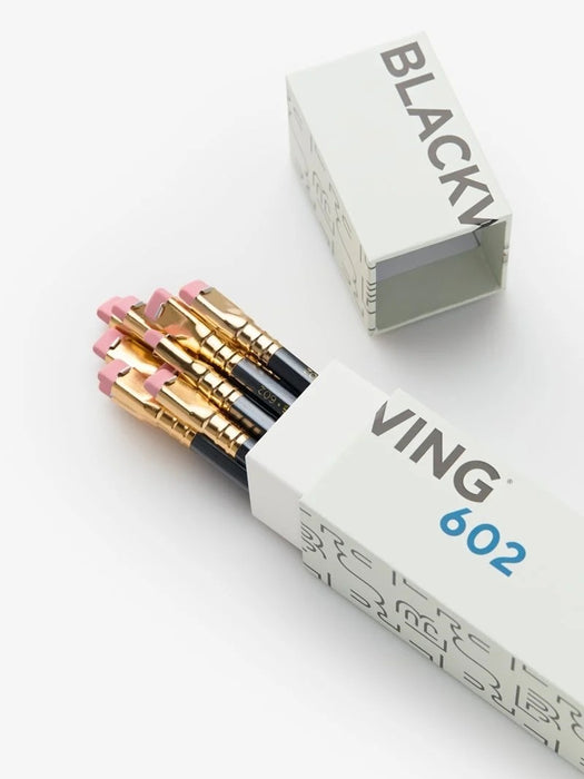 A set of 602 black pencils with gold ferrules and pink erasers, shown in their white patterned packaging alongside the open box lid on a clean white background.