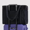 A black soft-sided duffel bag with a telescoping handle, shown resting on top of a purple rolling suitcase against a light gray studio background.