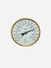A round analog thermometer with a gold-toned metal frame, white face, black pointer, and black printed temperature markings in Celsius and Fahrenheit, shown against a light gray background.