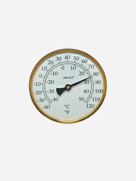 A round analog thermometer with a gold-toned metal frame, white face, black pointer, and black printed temperature markings in Celsius and Fahrenheit, shown against a light gray background.
