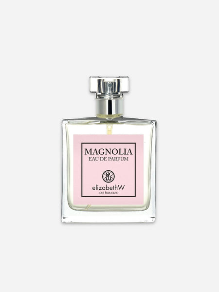 A clear glass perfume bottle with a silver cap and a light pink label reading 'MAGNOLIA EAU DE PARFUM' and 'elizabethW', centered on a light gray background.