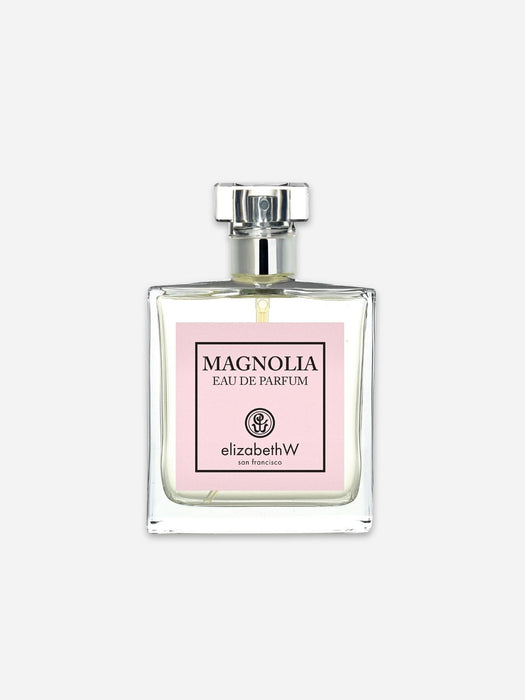 A clear glass perfume bottle with a silver cap and a light pink label reading 'MAGNOLIA EAU DE PARFUM' and 'elizabethW', centered on a light gray background.