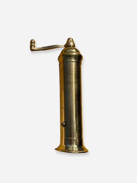 A vintage brass wall-mounted water pump or hydrant with a cylindrical body, engraved markings, and a curved hand crank extending to the left, shown against a plain light gray background.