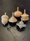 five hand turned wooden spinning tops on a dark wood background
