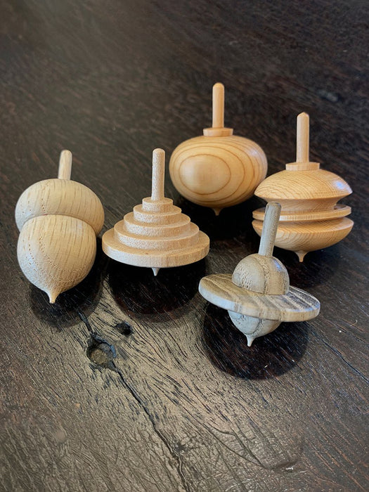 five hand turned wooden spinning tops on a dark wood background