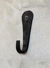 A rustic black metal hook with a distressed finish, mounted on a textured off-white plaster wall.