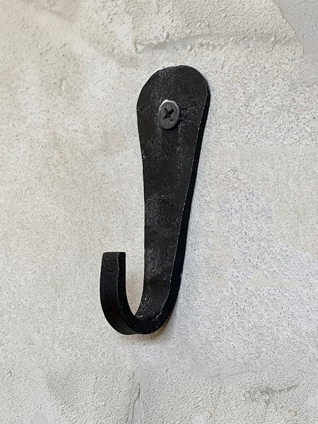 A rustic black metal hook with a distressed finish, mounted on a textured off-white plaster wall.