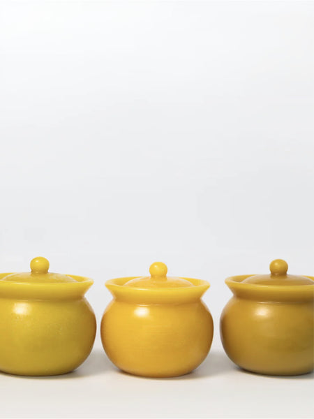 Three small round lidded jars in a matte mustard yellow color, arranged in a row against a plain white background.