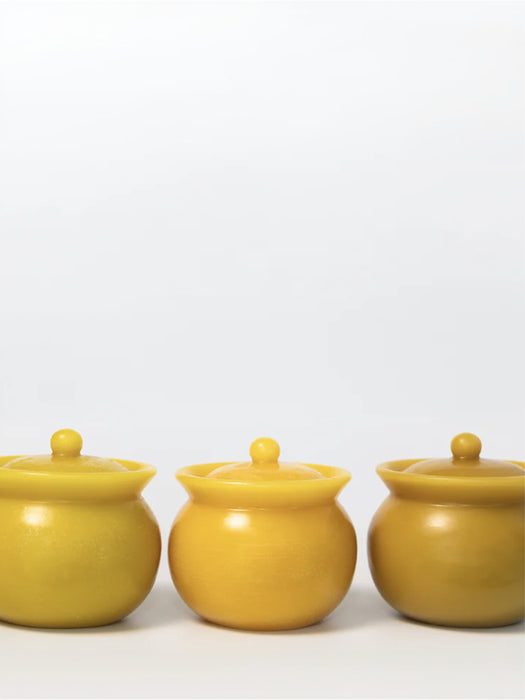 Three small round lidded jars in a matte mustard yellow color, arranged in a row against a plain white background.