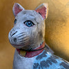 Wooden cat figurine with blue eyes and a pink collar against a yellow background