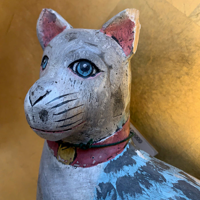 Wooden cat figurine with blue eyes and a pink collar against a yellow background