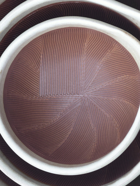 A close-up of a round brown ceramic plate with a textured, ribbed pattern and a white rim, nested inside other similar plates.