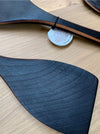 A close-up of a dark gray wood grain textured spatula, on a light wood background with a small white tag attached.