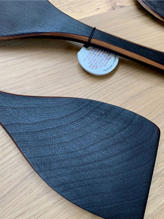 A close-up of a dark gray wood grain textured spatula, on a light wood background with a small white tag attached.