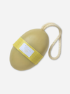 A natural soap latherer, an oval-shaped natural sponge with a cream-colored rope loop and a yellow ribbed band featuring a white brand label, shown on a light gray background.