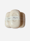 Three oval-shaped cream-colored soap bars wrapped in white paper bands labeled 'Magnolia', arranged in a fan-like composition on a light gray background.
