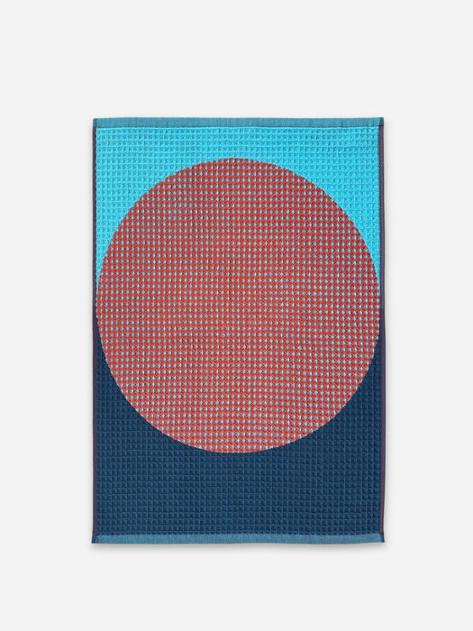 Waffle knit hand towel with a lighter blue on top and a darker blue on bottom with a large red circle in the center. 