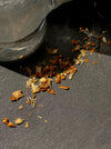 Dried orange and beige flower petals scattered on a dark gray surface beneath the edge of a clear glass container.