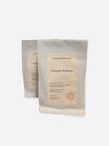 Two matte white pouches of herbal tea, with the front pouch labeled 'Leaves and Flowers Turmeric Wellness' standing in front of a second pouch on a light gray background.