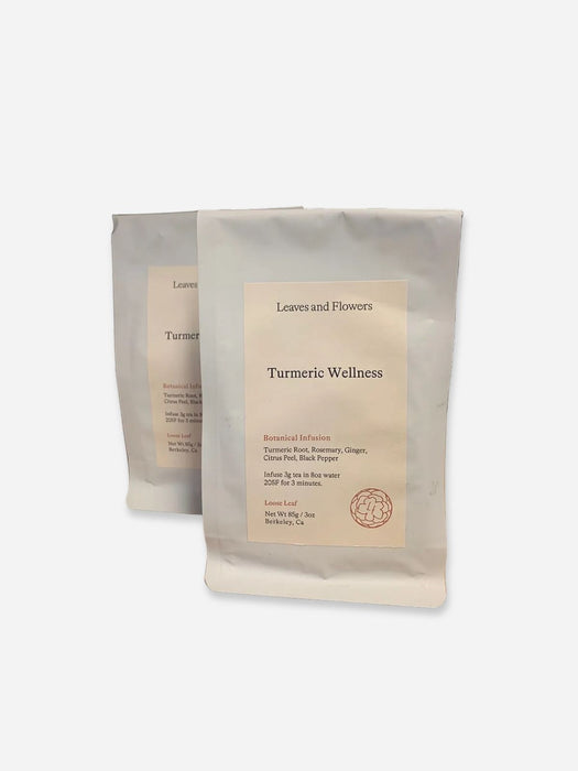 Two matte white pouches of herbal tea, with the front pouch labeled 'Leaves and Flowers Turmeric Wellness' standing in front of a second pouch on a light gray background.