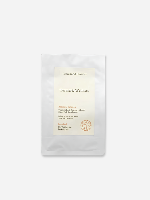 matte white pouches of herbal tea, with the front pouch labeled 'Leaves and Flowers Turmeric Wellness' standing in front of a second pouch on a light gray background.