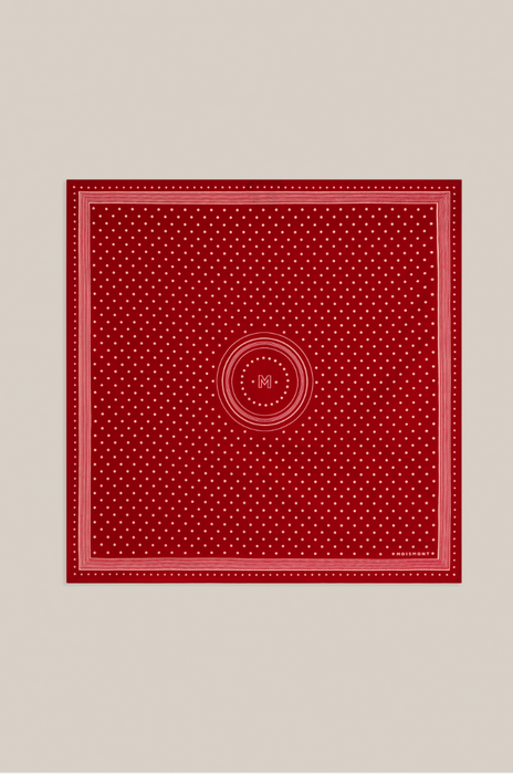 A square red scarf with a white micro-dot pattern, featuring a central circular motif and a decorative border, displayed flat against a neutral light gray background.