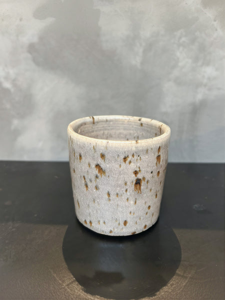 Handmade ceramic cup light grey with brownish speckles on the surface.