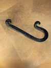 A dark metal J-shaped hook with a textured, hand-forged finish, resting on a textured gold surface.