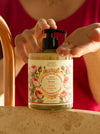 A person at a bathroom counter pumps liquid hand soap from a clear bottle with a black pump. The label reads 'Panier des Sens' and 'Rose'.