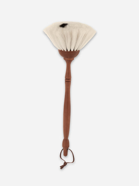 A handmade fan brush with a long brown wooden handle, a small wooden ferrule, and off-white bristles, shown against a light gray background.