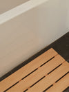 wooden slat bath mat on a dark floor in front of a white bathtub edge
