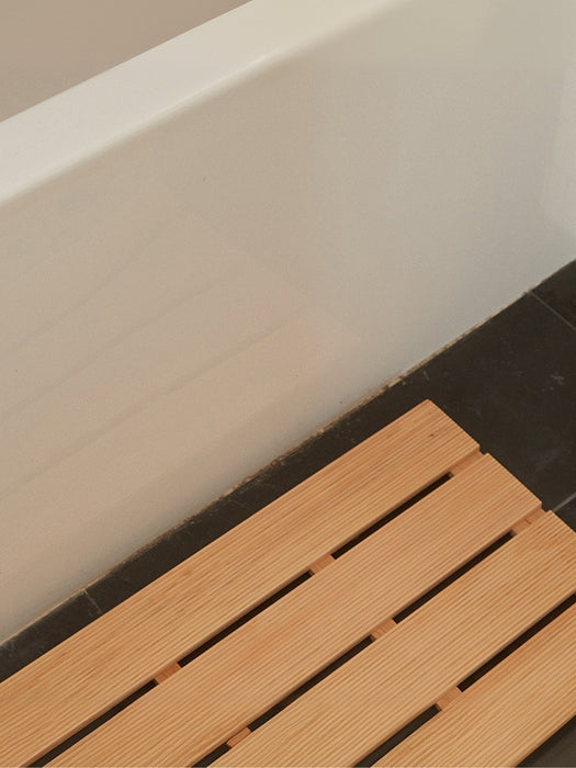 wooden slat bath mat on a dark floor in front of a white bathtub edge