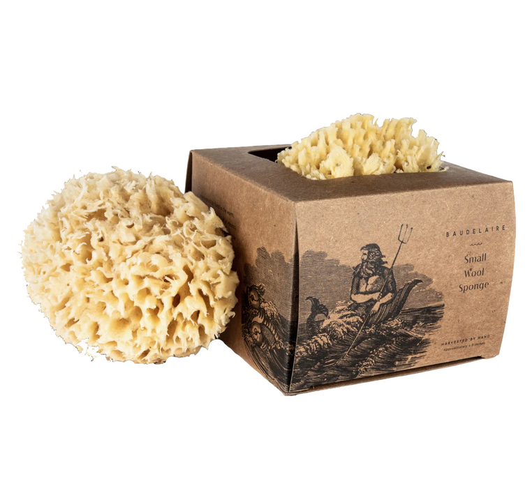 A small natural beige sea wool bath sponge displayed next to its brown kraft paper packaging box with an illustration of a figure holding a pitchfork. 