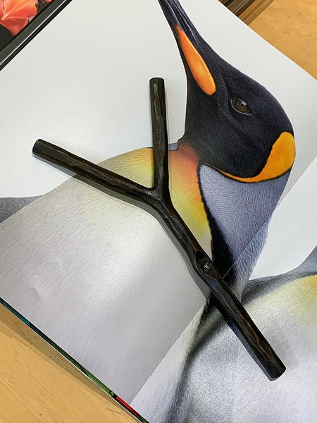 An iron branch-shaped bookmark displayed on top of a printed penguin illustration.